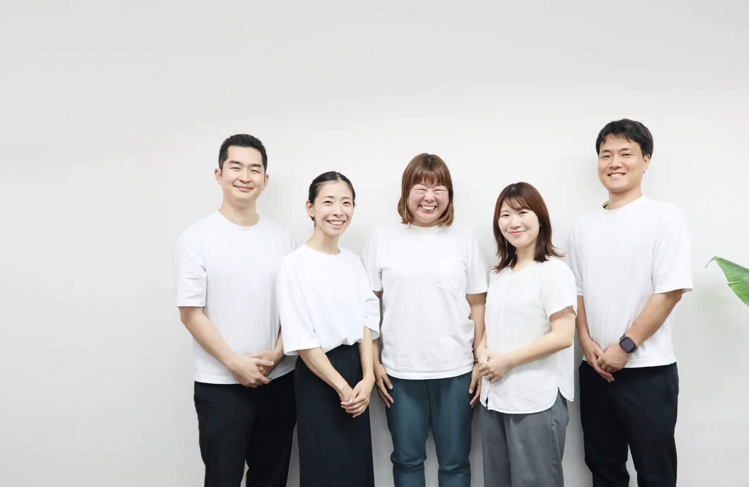 白いTシャツを着た5人のスタッフが並んで笑顔で立っている事業所の写真